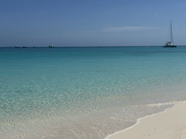 A serene view of a tranquil beach with crystal-clear waters and sailboats in the distance, perfect for a relaxing day by the sea.