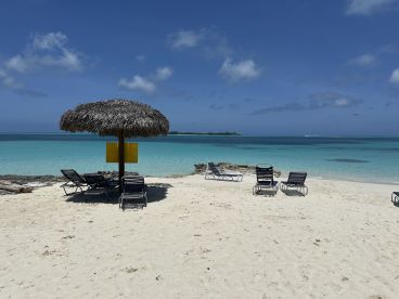 A serene beach scene featuring lounge chairs and a thatched umbrella overlooking turquoise waters, perfect for relaxation and sunbathing.