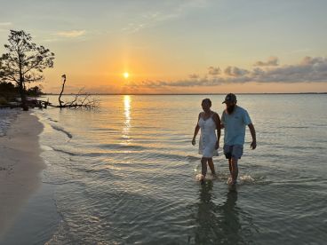 A couple enjoys a romantic stroll along the beach at sunset, creating a picturesque moment by the water's edge.