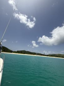 A serene view from the side of a yacht, showcasing clear turquoise waters and a sandy beach in the background — perfect for a relaxing day on the water.