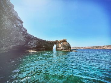 A stunning view of a natural rock arch along the coastline, showcasing the beauty of the surrounding waters — perfect for scenic boat tours and exploration.