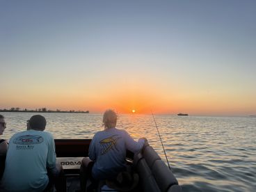 A group enjoys a serene sunset while fishing on a boat in Siesta Key, capturing the perfect moment for a memorable evening on the water.