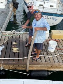 Two friends proudly display their catch of the day on the dock, celebrating a successful fishing trip. The backdrop features a boat, enhancing the maritime experience.