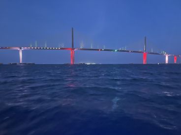 A stunning view of a brightly lit bridge at night, reflecting beautifully on the water — perfect for capturing the essence of a nighttime boating experience.