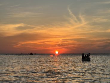 A picturesque sunset view with a boat silhouette and a group of people enjoying the serene waters — perfect for capturing memorable moments on a sunset cruise.