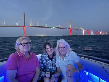 A joyful group of friends enjoys a night out on the water, with a beautifully lit bridge in the background, perfect for memorable boat outings.