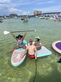 A lively group enjoys paddleboarding and swimming in shallow waters, showcasing a fun beach day filled with laughter and adventure.
