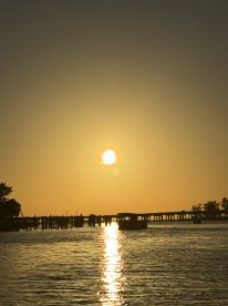 A serene sunset view over the water, with a silhouette of a dock and a boat gently reflecting the golden hues — perfect for capturing tranquil moments on the water.