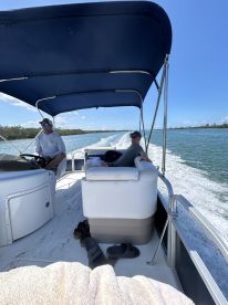 Two men relax in the helm area of a boat, enjoying a leisurely ride through scenic waters. The spacious seating and canopy provide comfort for a perfect day on the water.