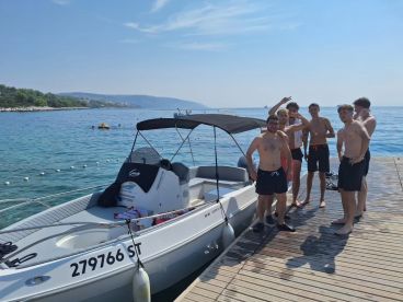 A lively group of friends enjoys a sunny day by the water, posing near their boat — perfect for summer adventures and fun on the beach.
