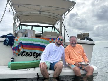 Two friends enjoy a relaxing moment on the back of a boat, sharing a meal and soaking in the serene waters — perfect for a day out on the water.