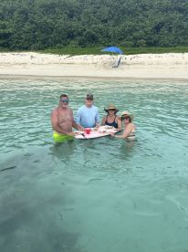 A lively group enjoys a sandbar stop, dining on delicious food while wading in the clear waters — a perfect setting for fun and relaxation.