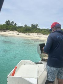 A person prepares fishing equipment on a boat near a beautiful beach, showcasing the perfect blend of adventure and relaxation in tropical waters.