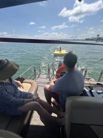 Guests relax on a boat while watching children enjoy a thrilling ride on a banana boat — a perfect day of fun and adventure on the water.