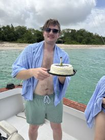 A man celebrates with a cake on a boat, showcasing a fun party atmosphere against a beautiful beach backdrop — perfect for memorable moments on the water.