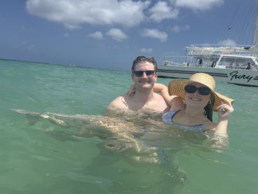 A couple enjoys a refreshing swim in crystal-clear waters with the Fury boat in the background, perfect for a fun day at the beach.