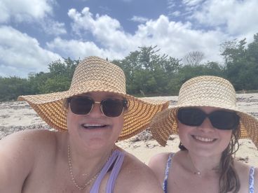 Two women enjoy a sunny day at the beach, wearing stylish sun hats and sunglasses — a perfect moment for family bonding and relaxation.