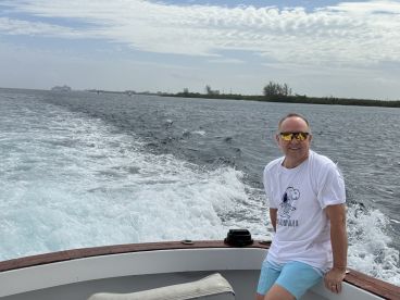 A man enjoys a sunny day on the water, smiling as he relaxes on a boat, showcasing the joy of boating adventures.