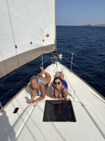 Two friends enjoy sunbathing on the deck of a sailboat, soaking up the sun and the ocean views — a perfect day on the water.