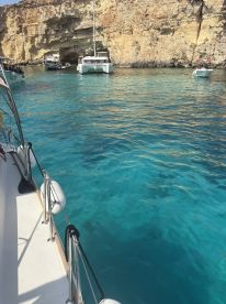 A scenic view of a catamaran anchored in crystal-clear turquoise waters, surrounded by stunning cliffs — perfect for exploring coastal caves and enjoying a day on the water.