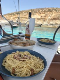 Delicious plates of pasta and bread are set up for an onboard dining experience, complemented by refreshing drinks — perfect for enjoying a meal while anchored in beautiful waters.