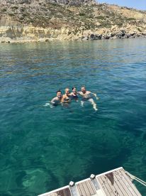 A cheerful group of friends enjoys a refreshing swim in crystal-clear waters, surrounded by stunning coastal scenery — perfect for summer adventures.