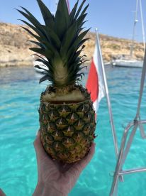 A refreshing pineapple cocktail is held against a backdrop of clear turquoise waters, perfect for enjoying tropical drinks on a boat.