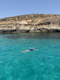 A child floats serenely in the crystal-clear waters near a rocky coastline, capturing the essence of a perfect summer day on the water.