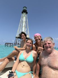 A joyful group poses in front of a lighthouse while enjoying their time on the water — a perfect snapshot of family fun and adventure.