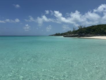 A stunning view of a tranquil beach with crystal-clear turquoise waters and lush greenery, perfect for a relaxing getaway or island exploration.
