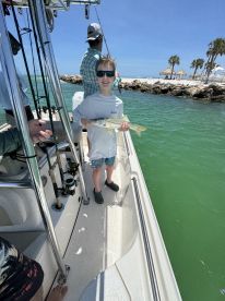 A young boy proudly holds up his catch while fishing from a boat, with a beautiful beach backdrop — a perfect family fishing adventure.