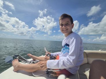 A young boy smiles while sitting on the edge of a boat, enjoying a sunny day on the ocean — a perfect moment for family adventures on the water.