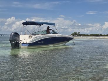 A NauticStar boat is docked in shallow waters, showcasing its sleek design against a backdrop of clear skies and gentle waves.