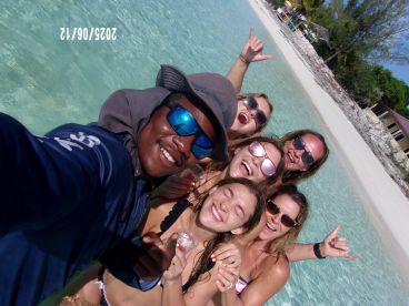 A joyful group of friends poses for a selfie in the clear waters of a tropical beach, celebrating their fun day under the sun.