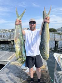 A proud angler displays his impressive catch of two mahi-mahi on the dock, showcasing the thrill of fishing adventures.