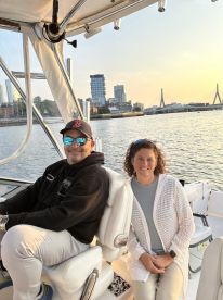A couple enjoys a scenic boat ride with a stunning city skyline in the background, perfect for romantic outings or sunset cruises.