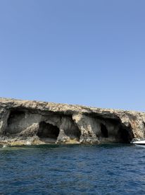 A stunning view of rocky caves along the coastline, with a boat anchored nearby, perfect for exploring hidden gems and enjoying the beauty of nature.