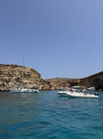 A lively scene featuring multiple boats anchored near a stunning coastline, with guests enjoying the sun and water activities — perfect for a summer adventure.