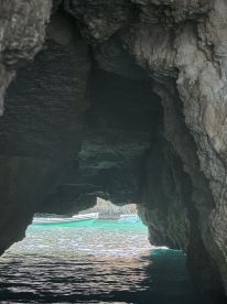 A stunning view through a natural cave opening, revealing boats anchored in turquoise waters — a picturesque scene perfect for exploring coastal wonders.