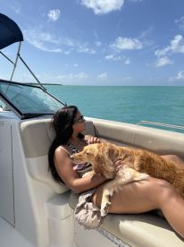 A woman enjoys a relaxing moment on a boat with her golden retriever, soaking in the sun and the beautiful ocean view.