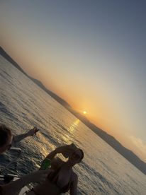 Guests enjoy a stunning sunset on the water, capturing the moment with drinks in hand — a perfect backdrop for summer celebrations.