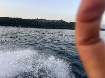 An unclear image taken from a moving boat, with a finger obstructing the view and a blurred background of water and land.