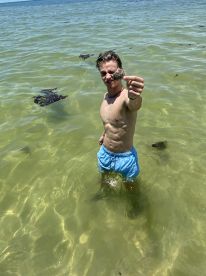 A young boy proudly holds up a shellfish while wading in shallow waters, showcasing a fun and adventurous day in nature.