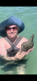 A woman holds a unique shell while wading in clear waters, showcasing a delightful human-animal interaction during a fun day at the beach.