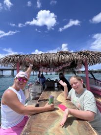 A lively group enjoys drinks aboard a boat with a thatched roof bar, perfect for celebrations and fun on the water.
