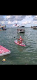 A woman paddleboards on a vibrant pink board in clear waters, showcasing the fun of on-water activities during a sunny day.
