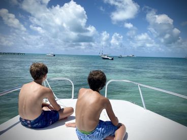 Two boys enjoy a serene moment on the bow of a boat, taking in the beautiful ocean view — a perfect snapshot of relaxation and adventure on the water.