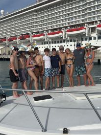 A cheerful group of friends and family poses on the deck of a boat, ready for a fun day at sea, with a cruise ship in the background.