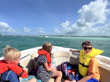 A group of children wearing life jackets enjoy a boat ride on a sunny day, surrounded by beautiful ocean views — perfect for family adventures on the water.