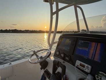 A serene view from the helm of a boat at sunset, showcasing the steering wheel and navigation equipment against a picturesque water backdrop.